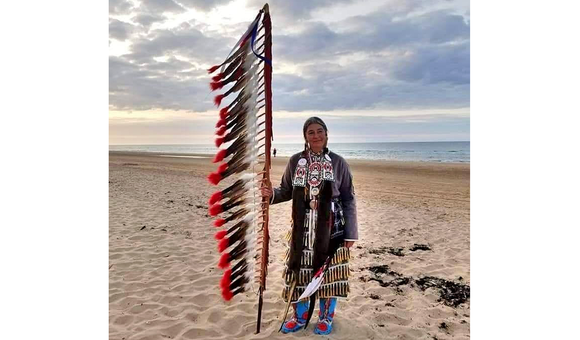 Command Sergeant Major Julia Kelly (U.S. Army retired), one of 80 Native American delegates to the 75th anniversary observance of D-Day, stands on Omaha Beach. Kelly holds an eagle feather staff, an American Indian symbol of respect, honor, and patriotism. (Courtesy of Julia Kelly)