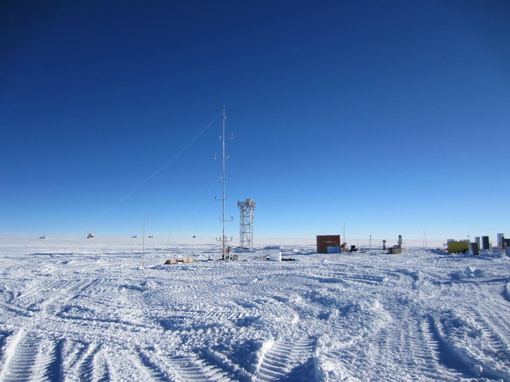 A view of Dome A site during daytime: a large expanse of snow, blue sky, and two metal structures rise out of the ground