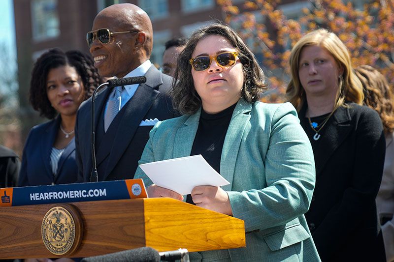 woman at a podium in front of NYC mayor