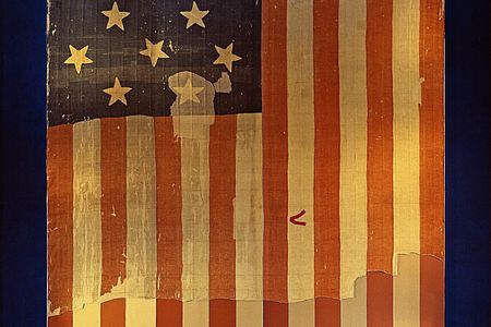 A piece of fabric has a design of alternating red and white stripes along with a dark blue rectangle featuring at least 14 white stars.