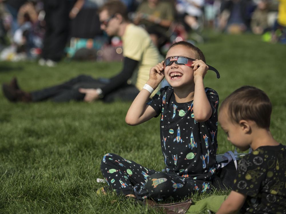 Little boy wearing eclipse glasses and smiling up toward the sky