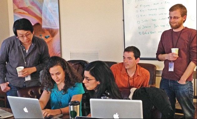 People crowding around laptops on a desk.