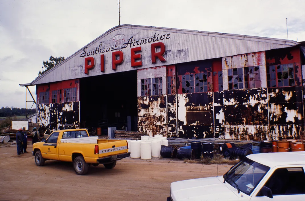 A rusty, broken hangar with two trucks parked in front