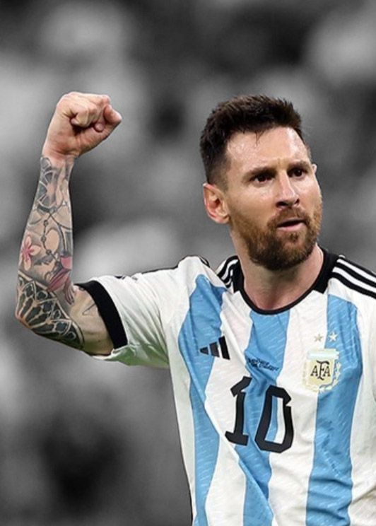 Messi, in blue and sky jersey number 10, holds up a power fist. He is in color and the background in black and white.