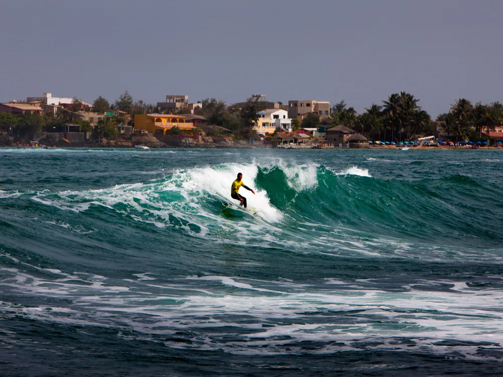 a surfer on a wave with some colorful buildings on the shoreline in the background