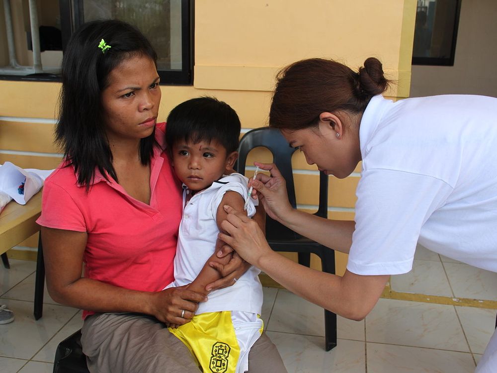 A woman in the Philippines sits with her four year old son as he receives a measles vaccine from a nurse in the aftermath of Typhoon Haiyan in 2013.