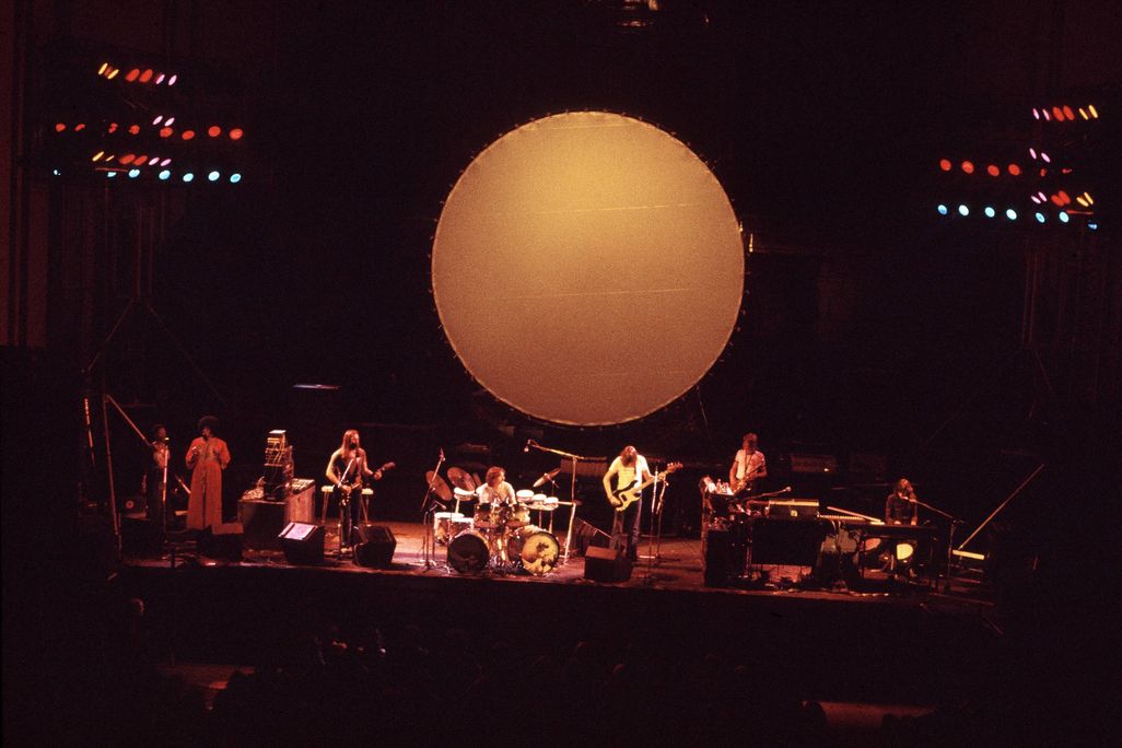 The band Pink Floyd plays on stage under an artistic rendering of a glowing moon