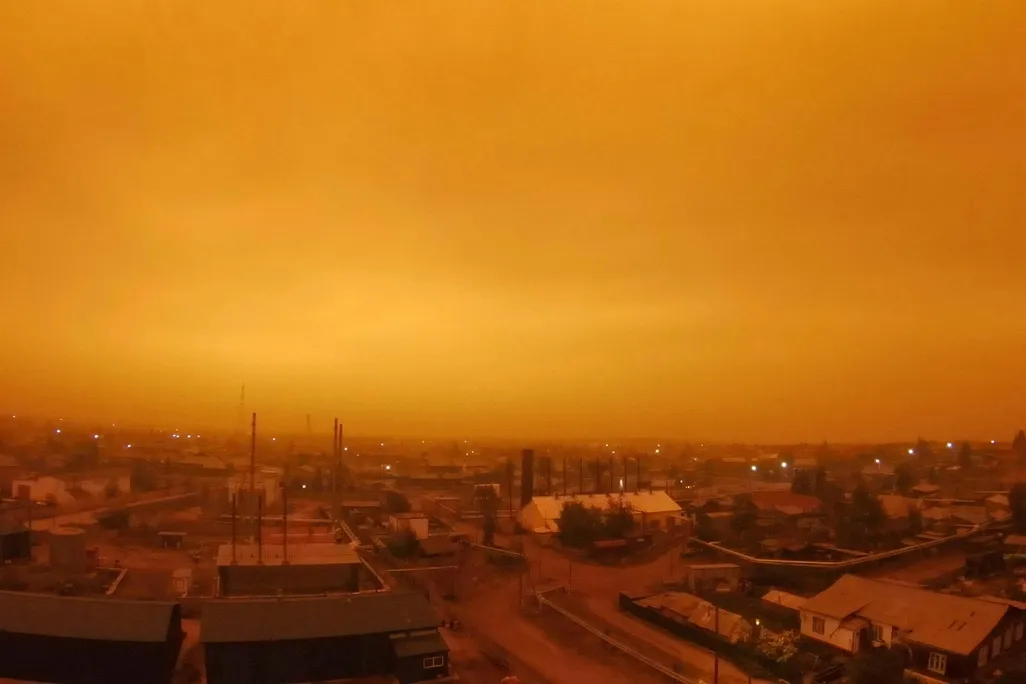 A photo of a small town in Russia. Its skies glowing an eerie amber color as wildfires continue to rage in Yakutia. 