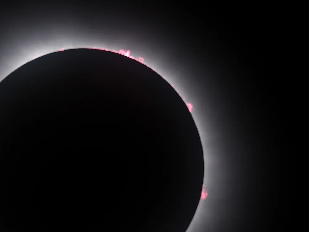 the eclipsed sun in the lower left of the frame shows the corona and some red bits of plasma