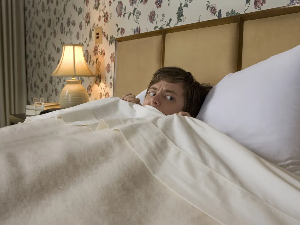 Man in bed with covers pulled up looking scared