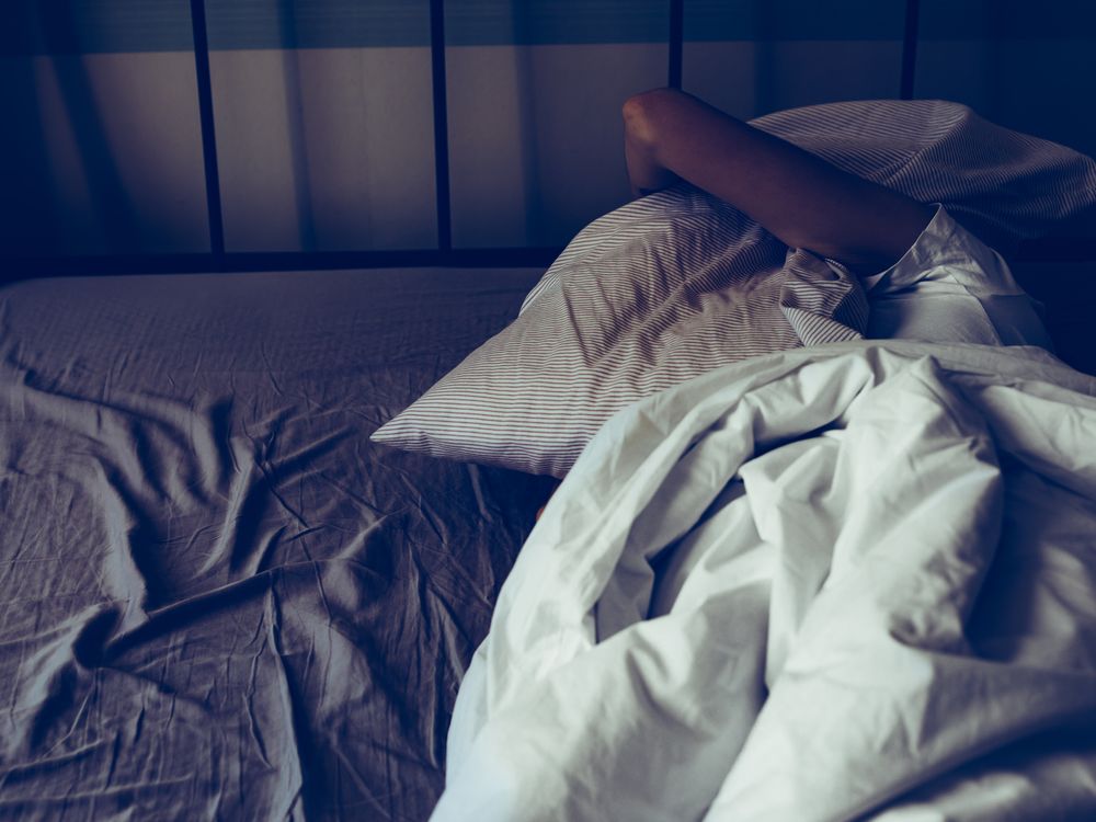 A person lying in bed holds a pillow over their head as they struggle to sleep