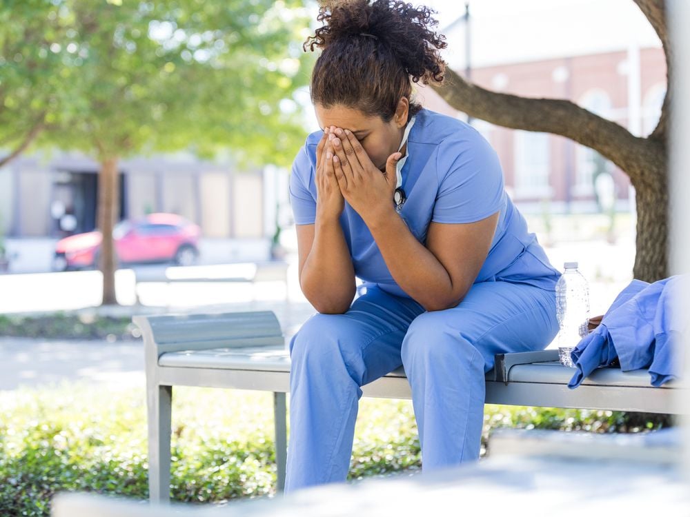 A healthcare worker sits outside with her head in her hands