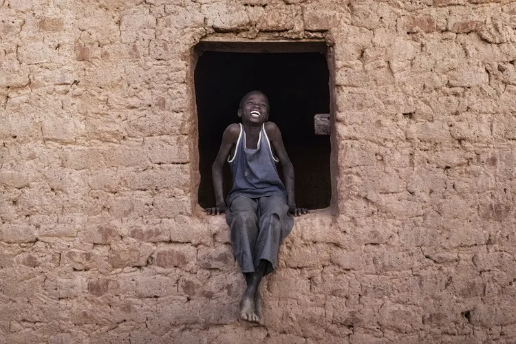 A teenage young African boy sits in a empty windowsill