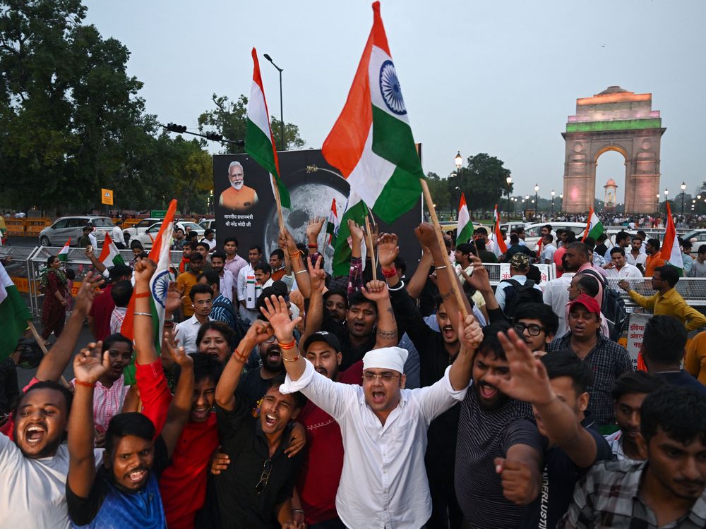 People hold their arms in the air and wave Indian flags as they celebrate the moon landing