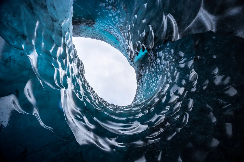 Within one of Iceland’s largest glaciers, walls of ice frame a slice of sky, forming the outline of an eye. This remarkable natural formation melted in 2024, a fleeting masterpiece sculpted by time and now lost.