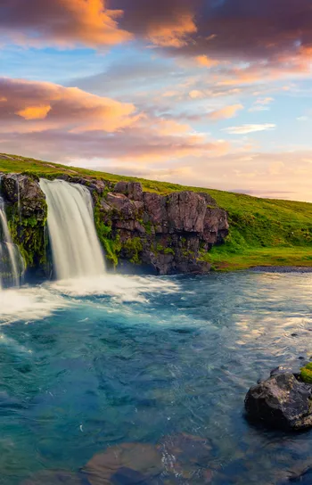 Private Jet Journeys - a picturesque sunset view of a river, waterfall and grassy hills.