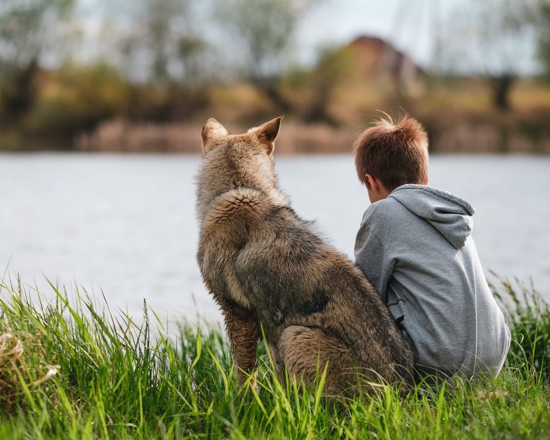 A boy and a dog sit next to a body of water.