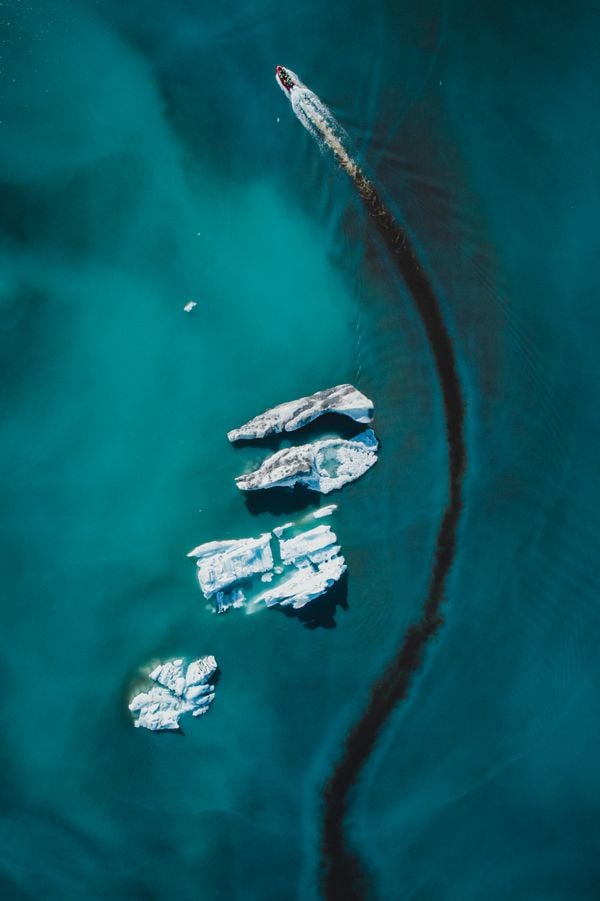 A boat glides through a glacial lake in Iceland. As it carves through the water, it parts the opaque, blue surface water, exposing the clear dark water beneath.