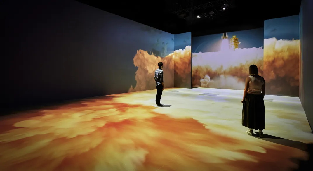 People standing in exhibit space with imagery on the walls and ceilings