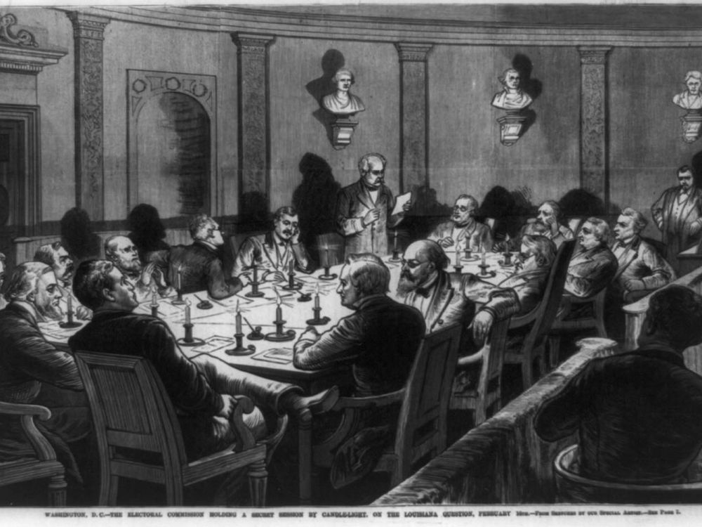 A black and white depiction of a group of men, sitting at a table in a formal room illuminated by candlelight on the table