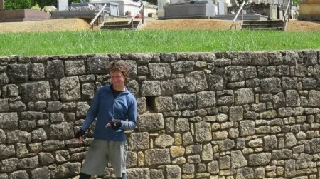 The author points directly at the hole in a rock wall in Groléjac where he left two cans of strong beer. Come get them.