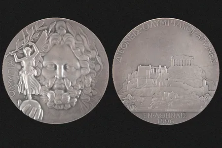 One side of the silver medal depicts Zeus holding Nike in the palm of his hand, while the other side features the Acropolis in Athens.