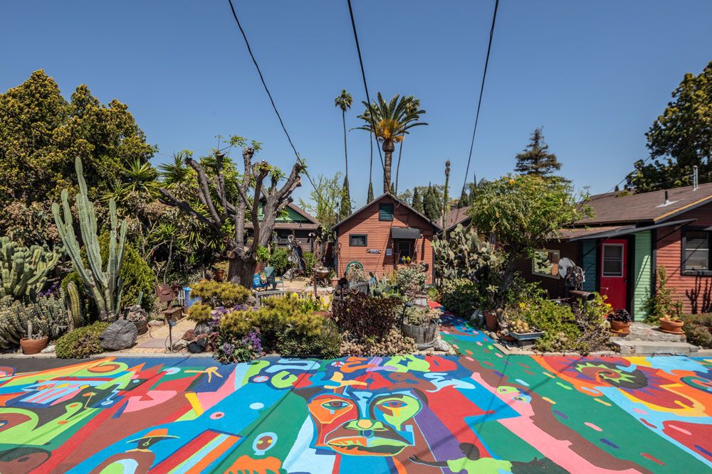 A brightly colored sidewalk in front of a few small houses, surrounded by lush vegetation