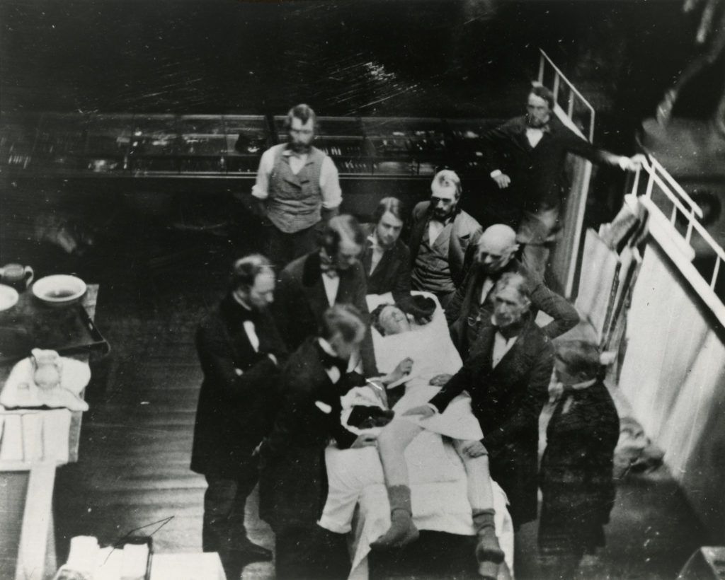 An 1847 photo op at the Ether Dome. Surgeon John Collins Warren holds the patient’s legs. William T.G. Morton is at the patient’s head, administering ether.