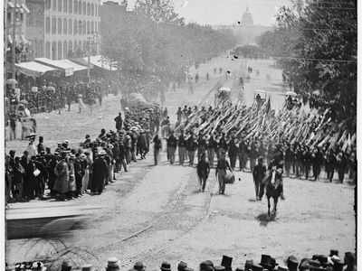 An infantry unit with bayonets marched down Pennsylvania Avenue in May 1865. They are followed by three ambulances.