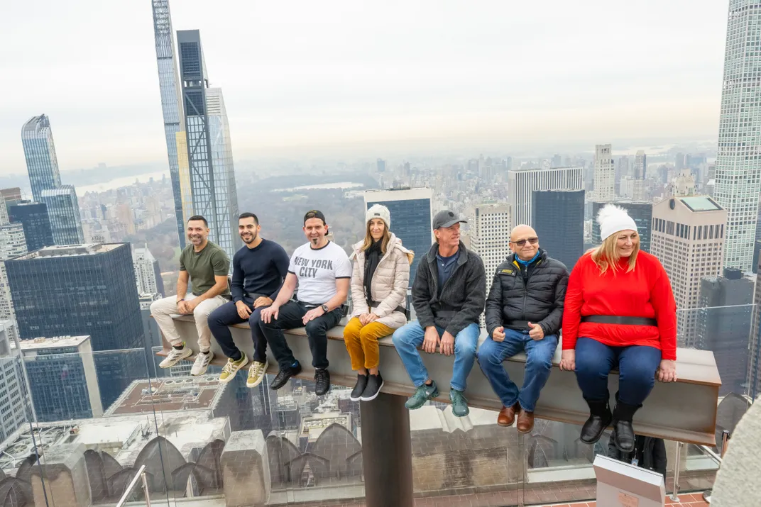 Row of people sitting on a beam with views of NYC in the background