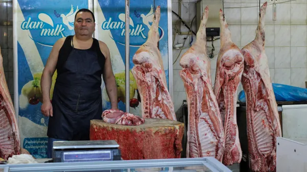 A butcher poses with meat carcasses at Tashir Bazaar in Yerevan, Armenia thumbnail
