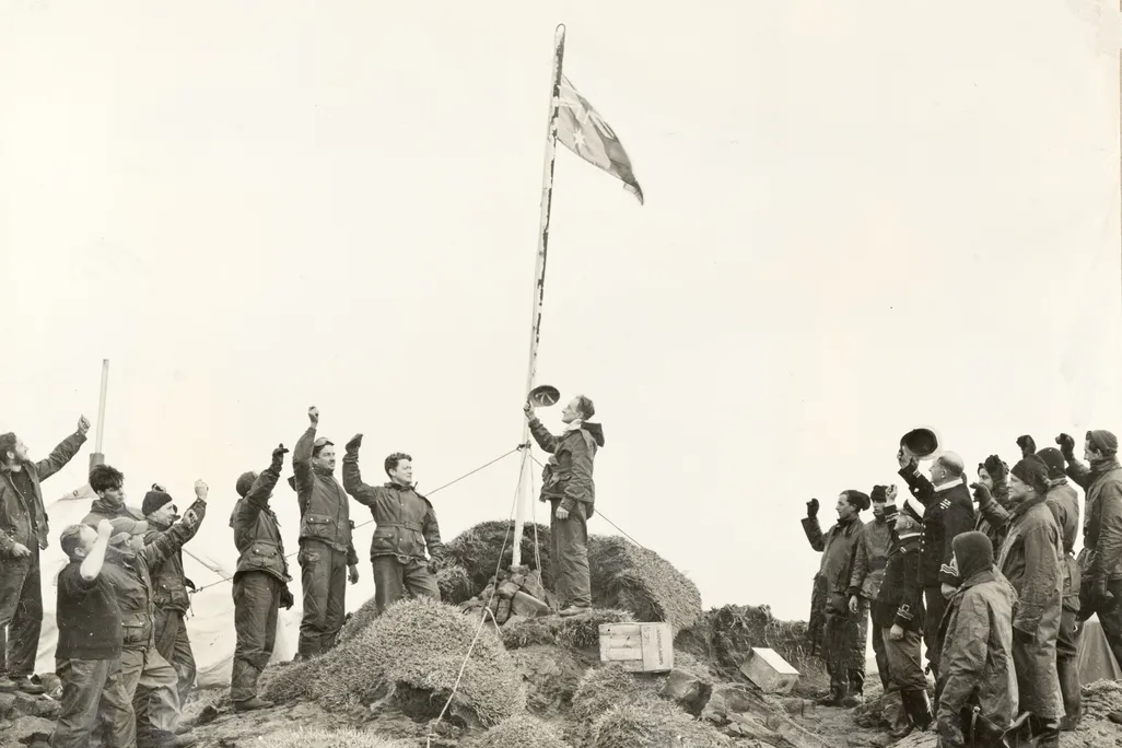Black and white photo of men standing around a flag