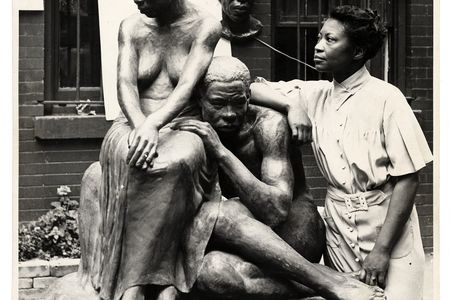 A black and white photograph of artist Augusta Savage standing next to her sculpture