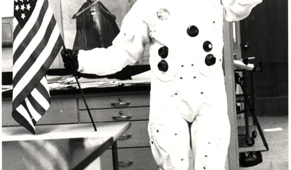 Informal classroom portrait of teacher Herbert Stephen Desind (1945-1992), wearing a reproduction Apollo-era spacesuit, holding an American flag; circa 1980s.  Desind was a space flight aficionado, and his collection of photographs of aircraft and spacecraft was donated to the National Air and Space Museum in 1997. This image is part of the Herbert Stephen Desind Collection.