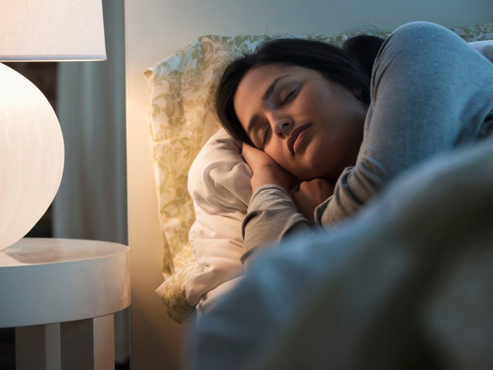 A woman sleeping in bed with a bedside lamp lit nearby