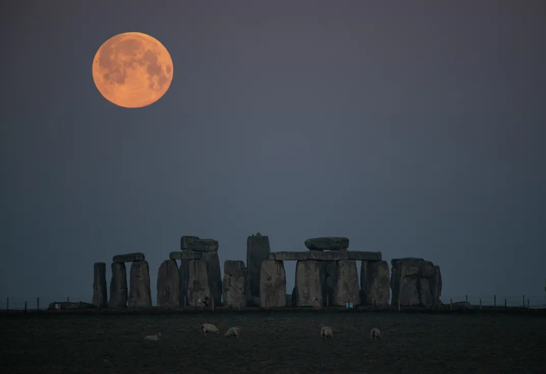 full moon looking orange over stonehenge monument
