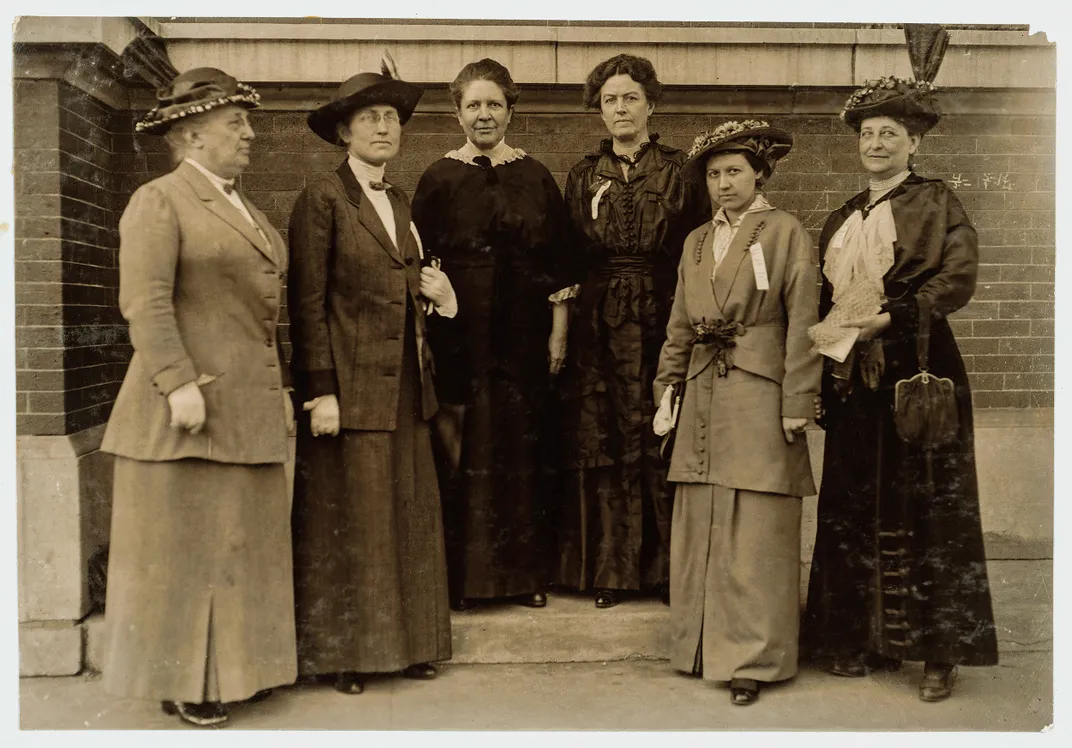 a group photo of women in formal dresses and hats