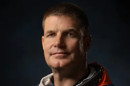 Dramatically-shot portrait of a white male astronaut in an orange spacesuit.