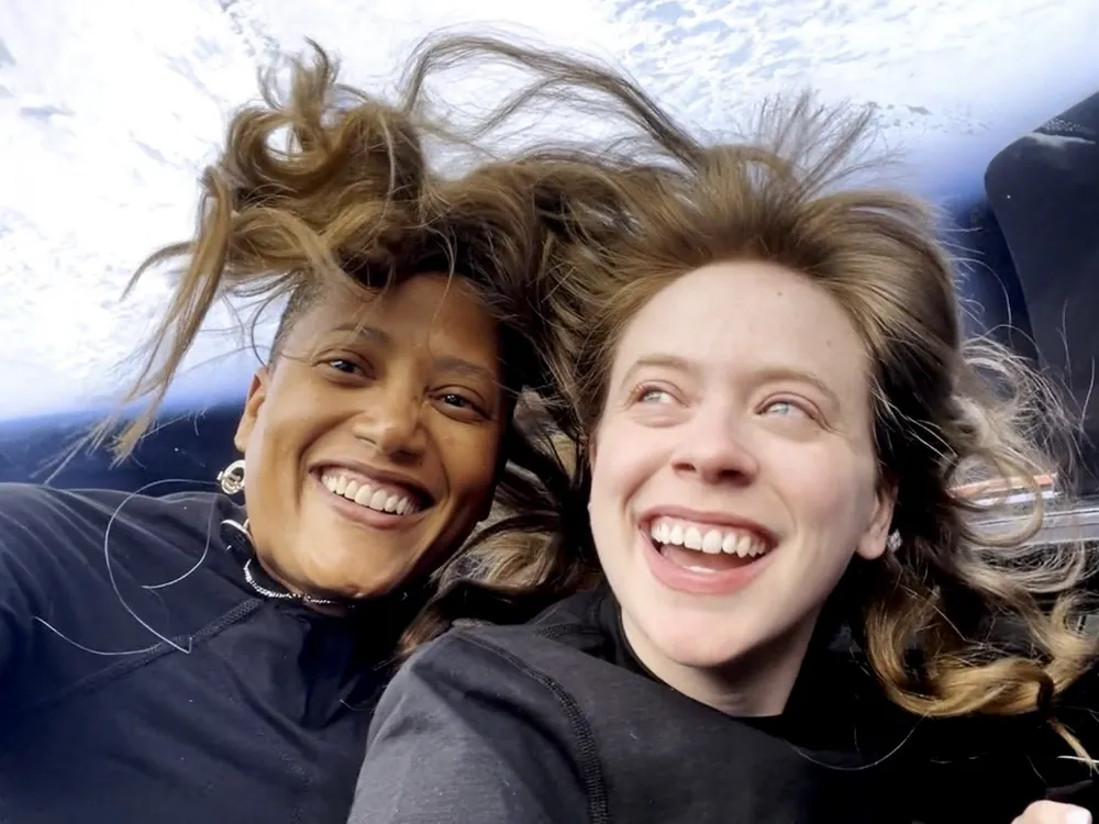 Two astronauts in space with their hair standing up and the Earth behind them
