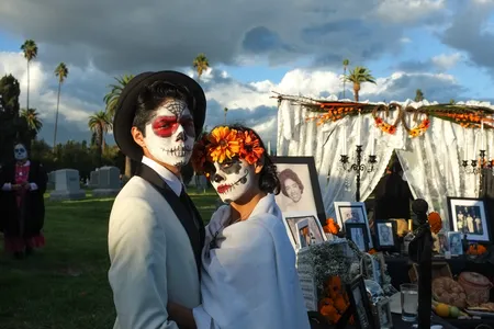 A couple visits a cemetery during Day of the Dead, against the backdrop of storm clouds.