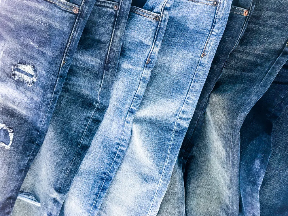 An assortment of different blue jeans laid on top of one another, including dark wash, light wash, and some with rips 