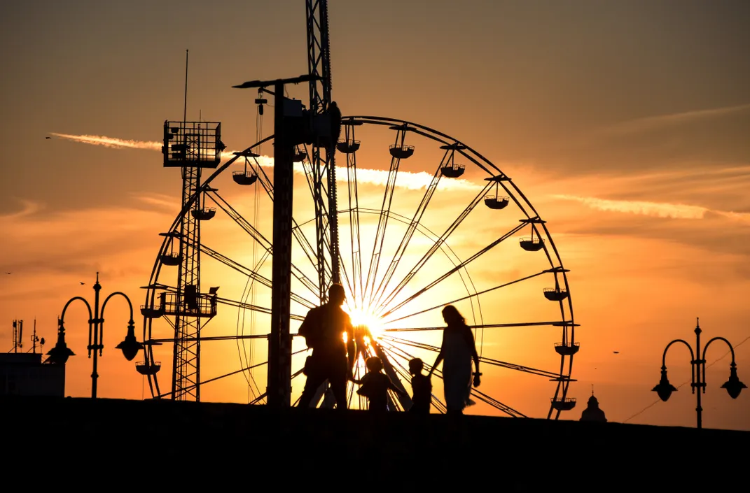 A family walks near a ferris wheel at sunset