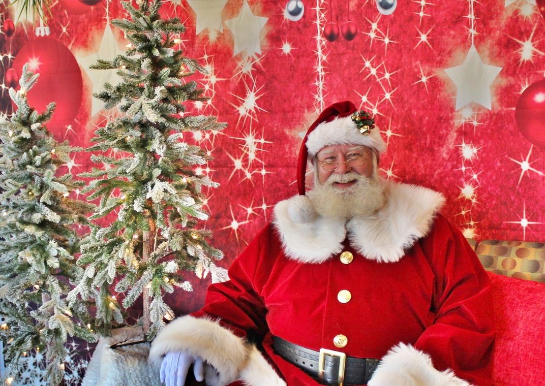 Santa Claus sitting next to Christmas trees