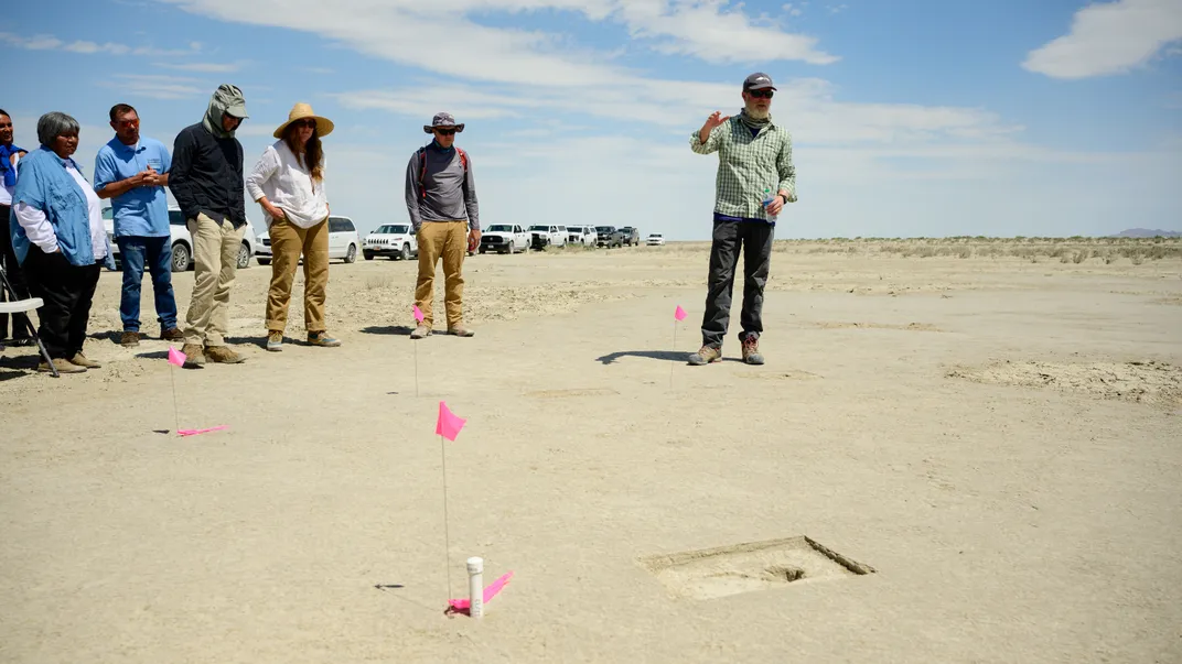 A group of people stands around a footprint, which is marked with a flag