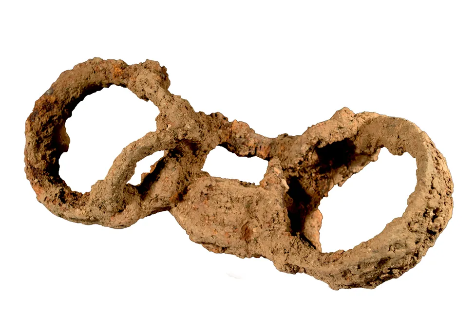 An image of a very rusted pair of shackles, two circles connected by a padlock that would have encircled someone's ankles