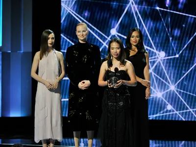 Winner Hillary Andales accepts her “science Oscar” from  actress Lily Collins (left) and philanthropist Julia Milner (next to Collins), as her stage escort waits.