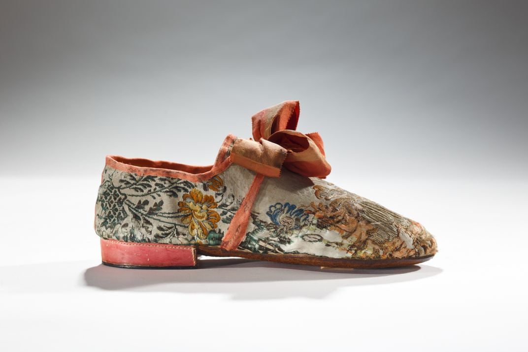 A man's shoe whose low heel conveyed it was masculine and whose expensive fabric and bow showed its owner was upper class