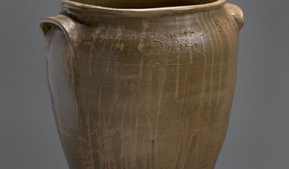 A brown, ceramic vessel with an inscription and the artist's name "Dave" carved around the opening.