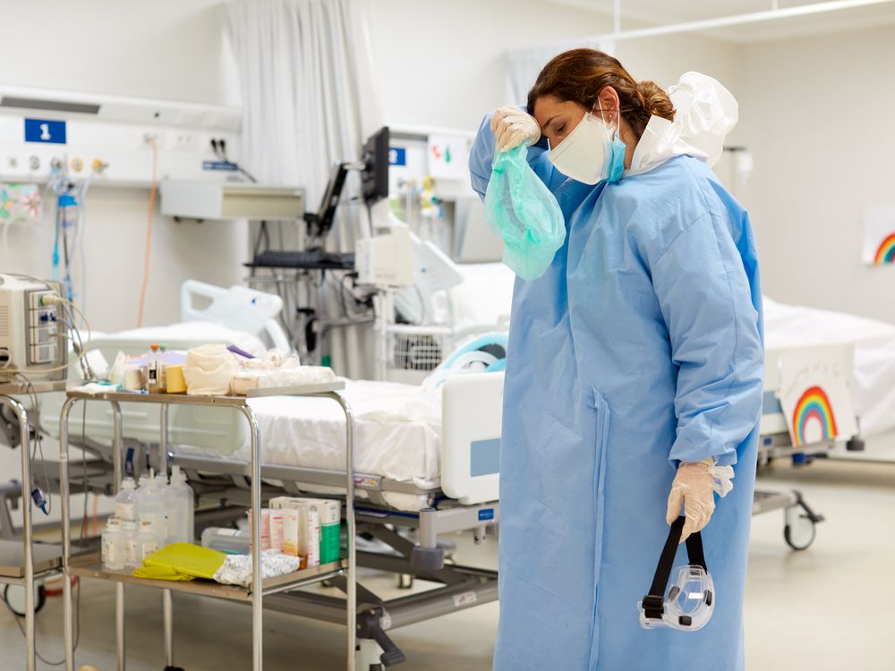 A female ICU doctor with a mask and gown wiping her forhead