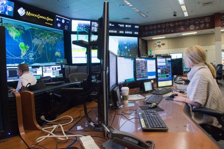 For three years, Lauren Cooper has been an ISS operations engineer. In the Johnson Space Center mission control room, she remains alert (note coffee cup) through eight-hour shifts.